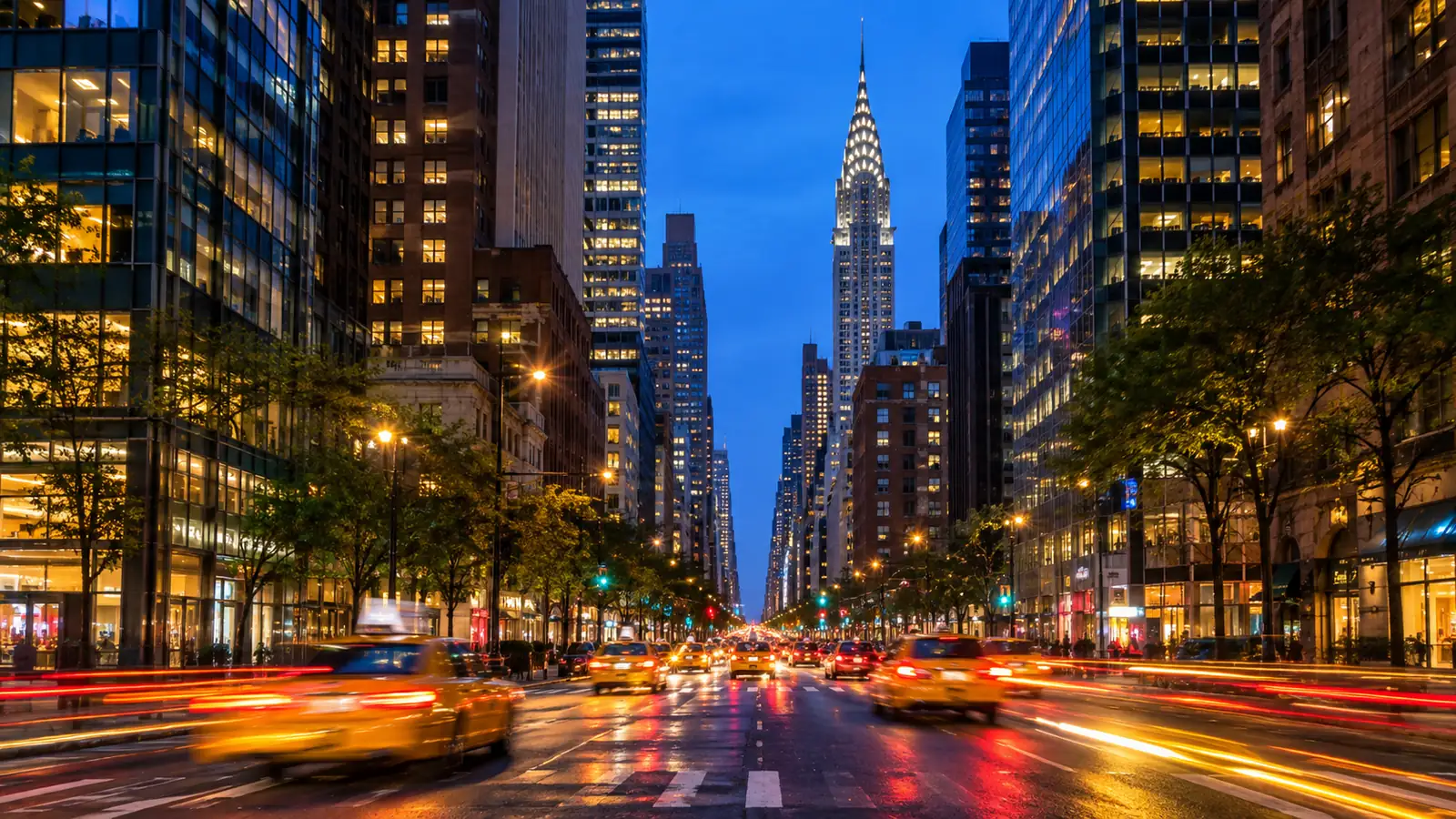 Yellow taxis on a Manhattan avenue at dusk under glowing skyscrapers
